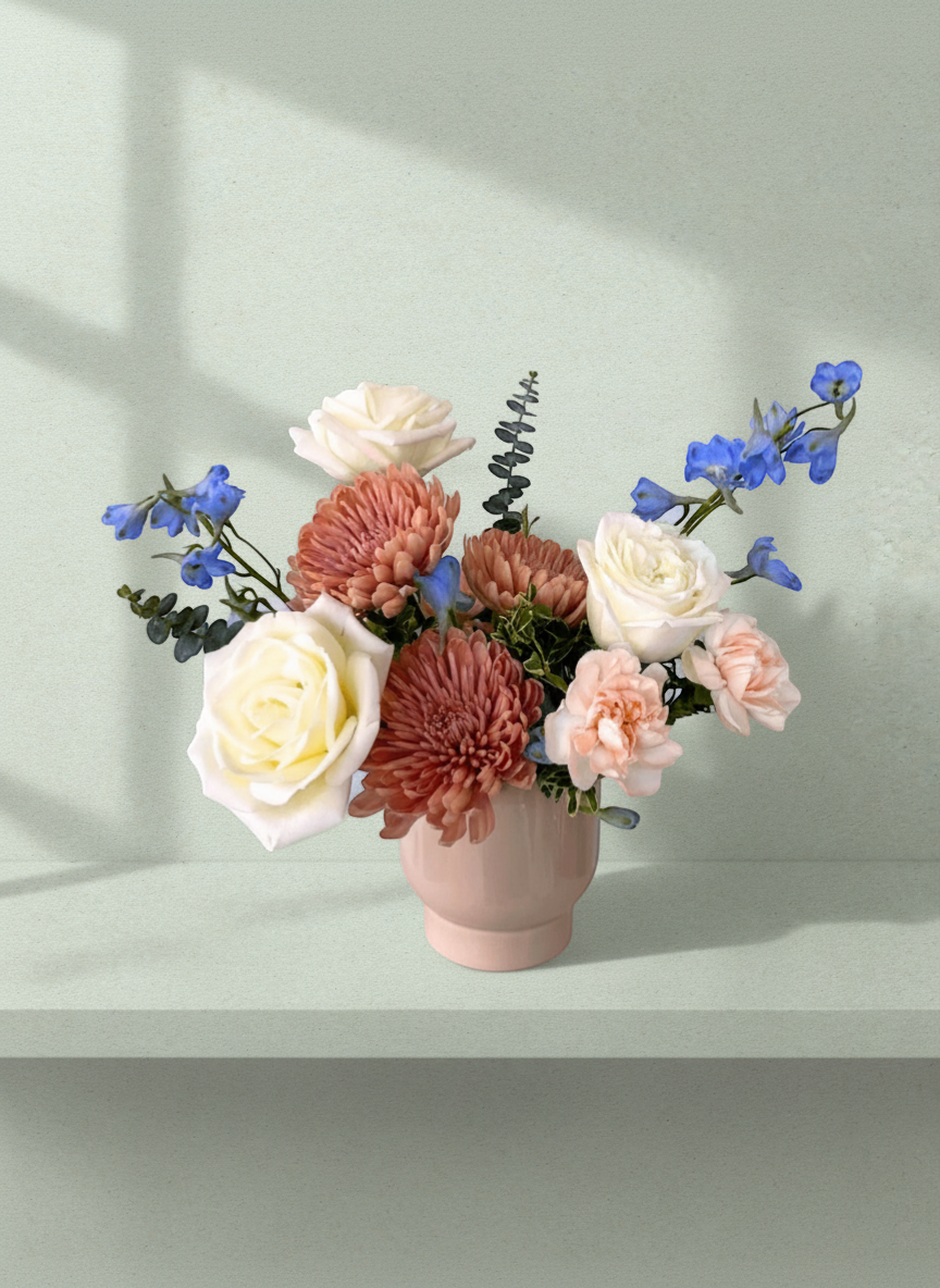 Lakewood Florist Easy Love arrangement: cream roses, coral mums, peach carnations, blue delphinium, and eucalyptus in a pink vase.