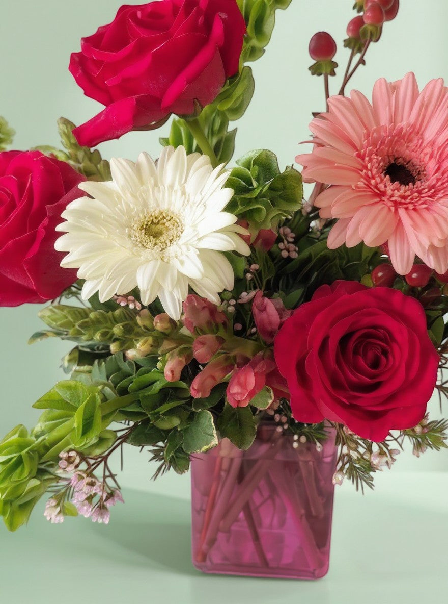 Lakewood Florist Love is in the Air arrangement: red roses, white daisy, pink gerbera, snapdragons in a pink vase.