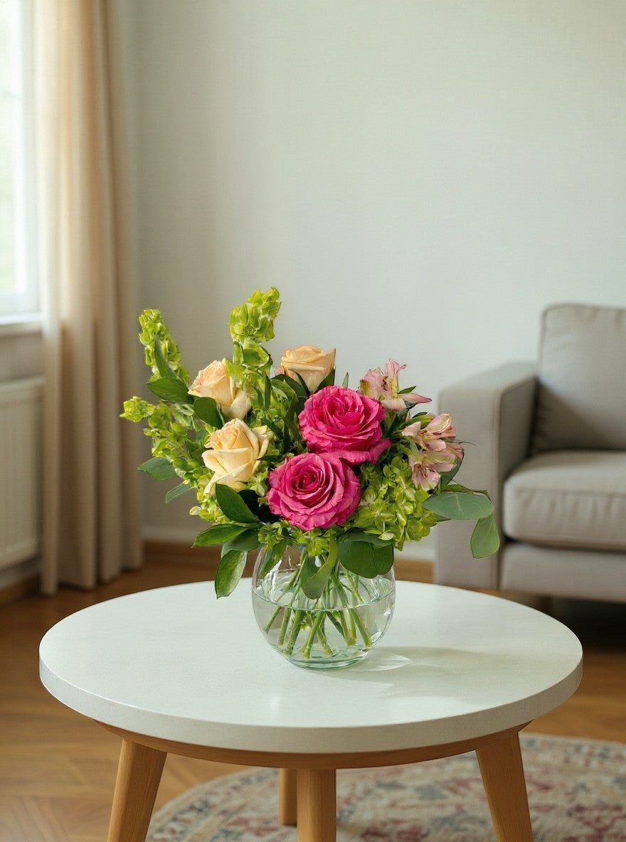 Lakewood Florist bright pink and peach roses with green foliage in a glass vase. A vibrant floral arrangement.