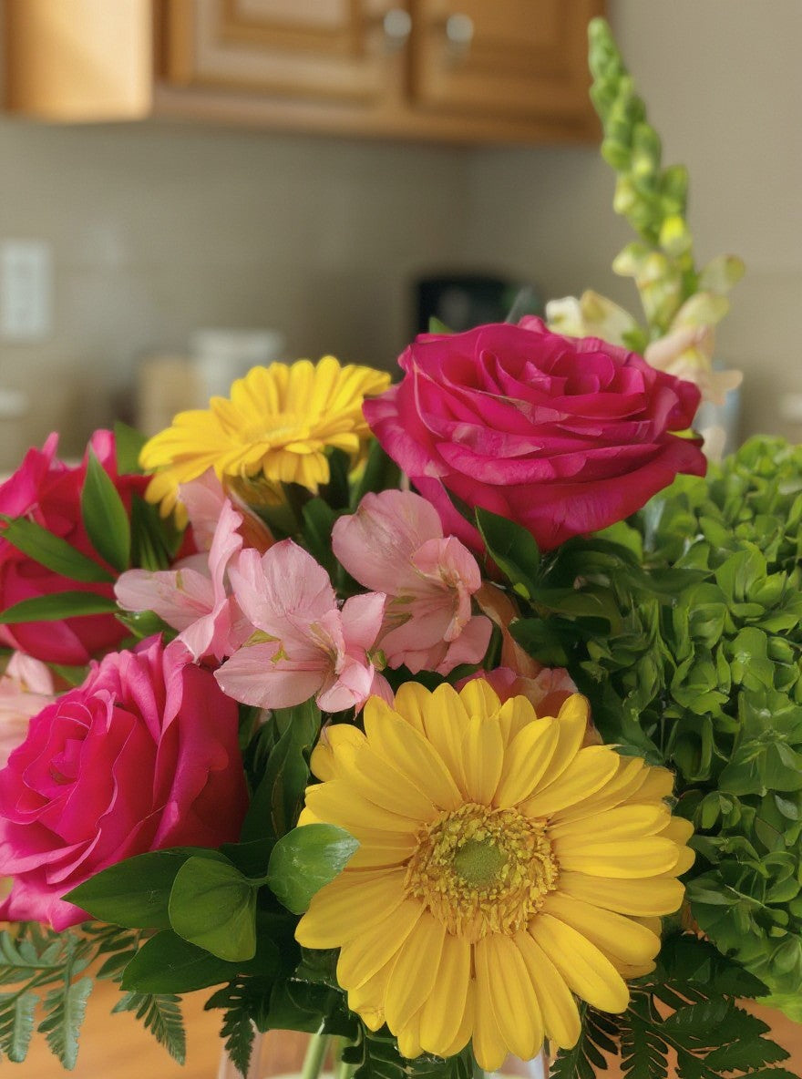 Lakewood Florist vibrant floral arrangement with pink roses, yellow gerberas, and green accents in a glass vase.